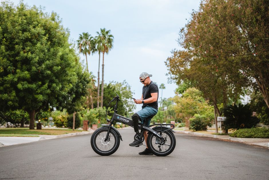Caucasian man with a prosthetic leg stands on a bike in a park, using his phone.