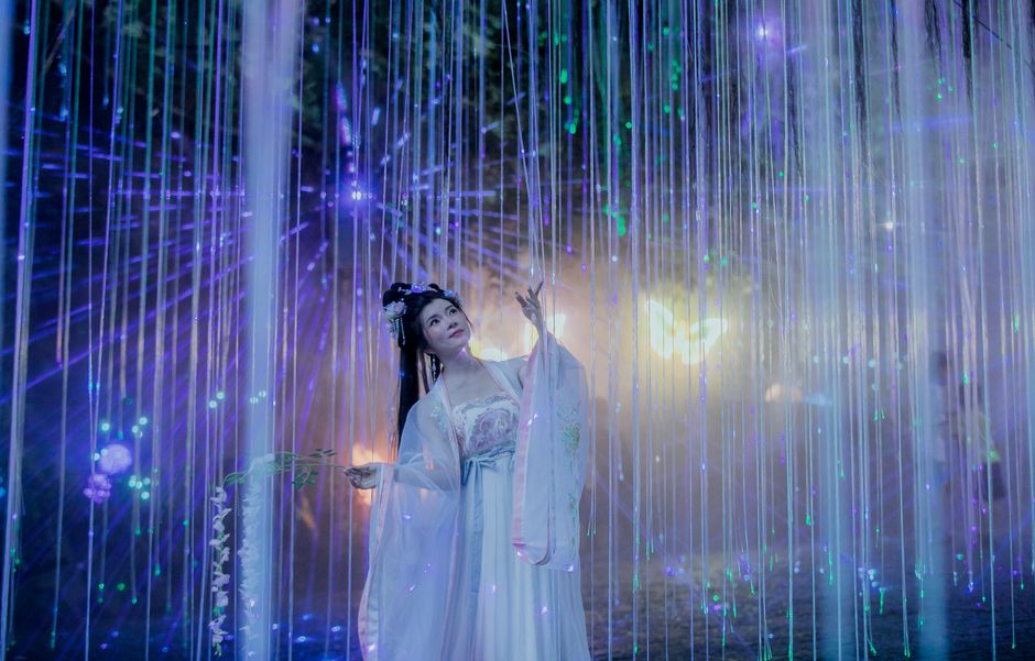 An Asian woman dressed in traditional attire, immersed in an illuminated fantasy scene with vibrant lights.