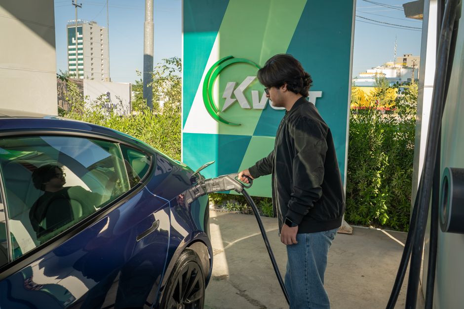 Young man charging a Tesla Model 3 at an outdoor electric vehicle station during the day.